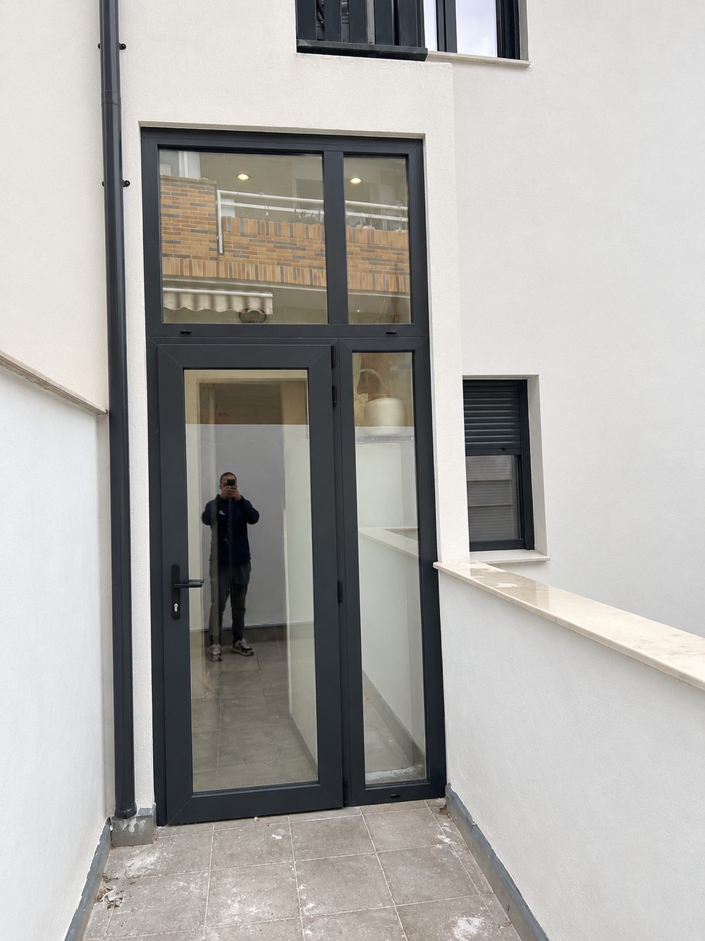 Puerta de acceso acristalada en aluminio antracita con fijo lateral y montante superior, en el patio de una vivienda