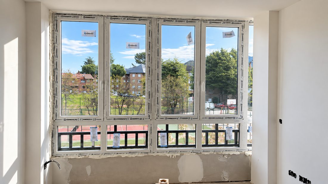 Ventanal de cuatro hojas oscilobatientes en PVC blanco, recién instalado y aún con los protectores, en una vivienda en obra