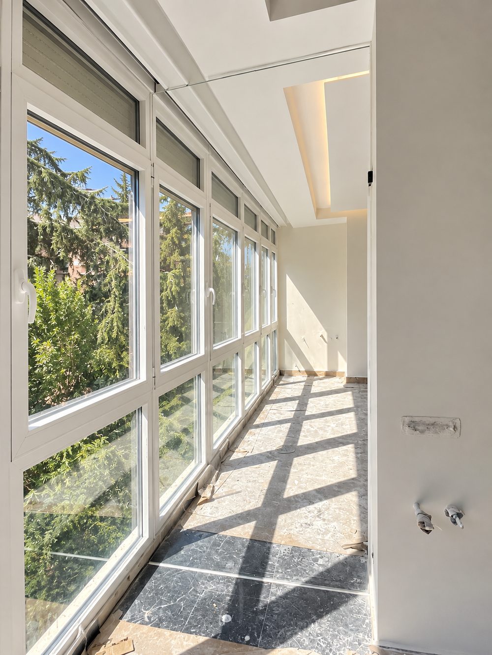 Galería corrida acristalada con ventanas correderas blancas y persianas, en una vivienda en obra
