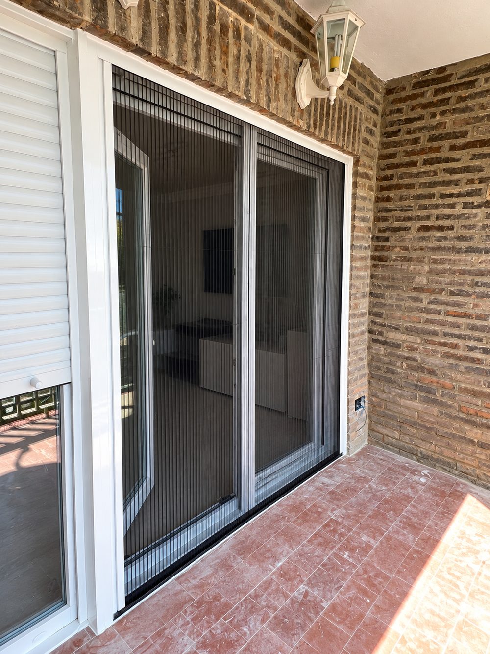 Mosquitera plisada de dos hojas instalada en la puerta corredera que da al porche de una vivienda