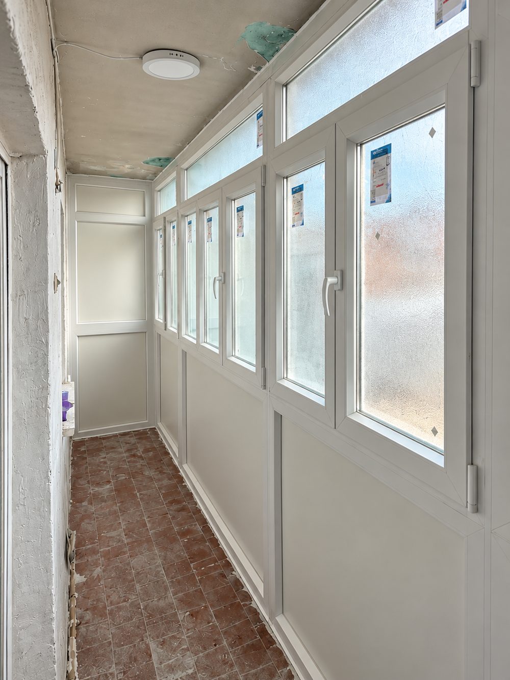 Galería cerrada con ventanas abatibles de PVC blanco, zócalo opaco y puerta de acceso, recién instalada