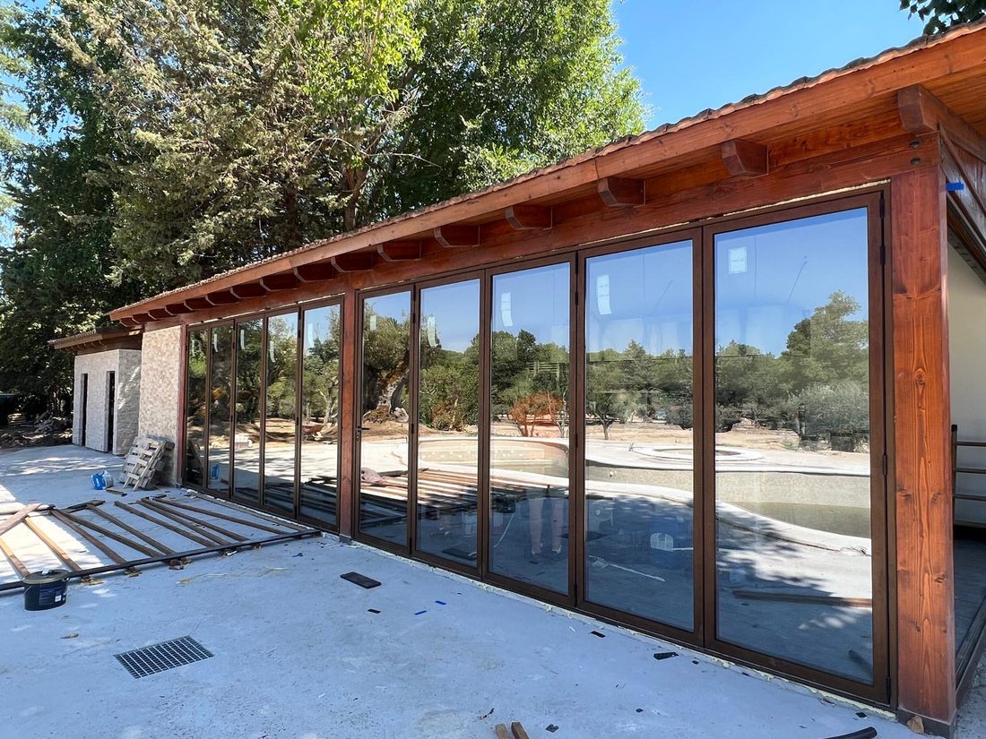 Cerramiento acristalado de gran formato con perfilería en acabado madera, montado bajo el porche de una vivienda