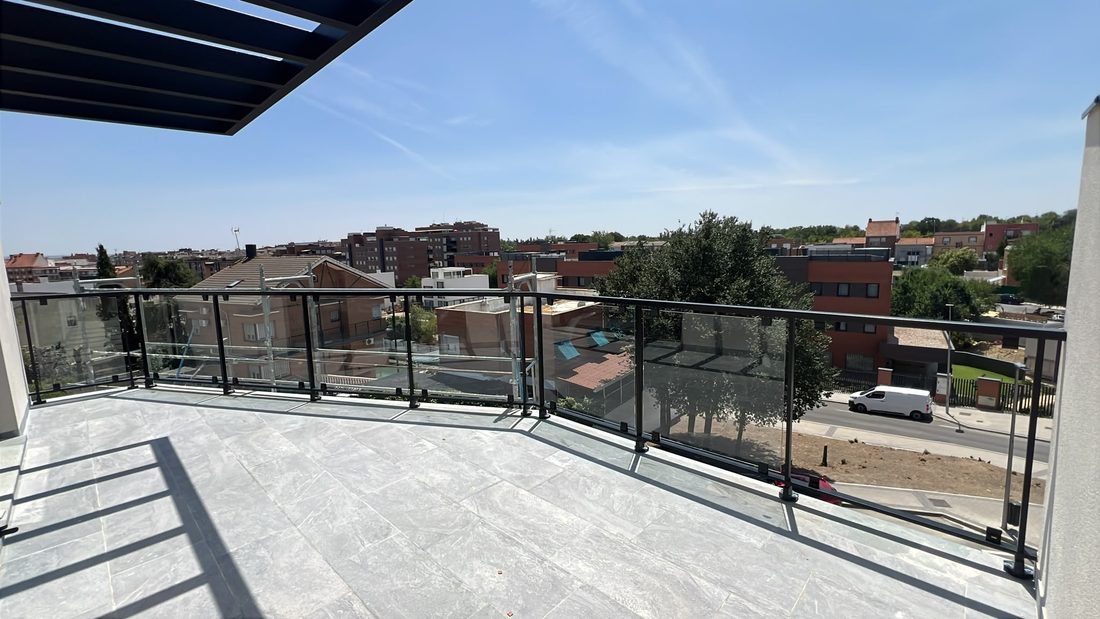 Terraza con barandilla de vidrio con perfilería oscura y pérgola de lamas, con vistas a la ciudad